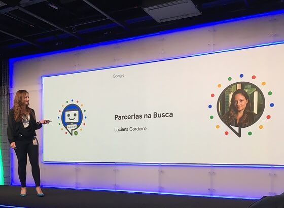 Funcionária Google Luciana Cordeiro na frente de telão com texto Parcerias na Busca